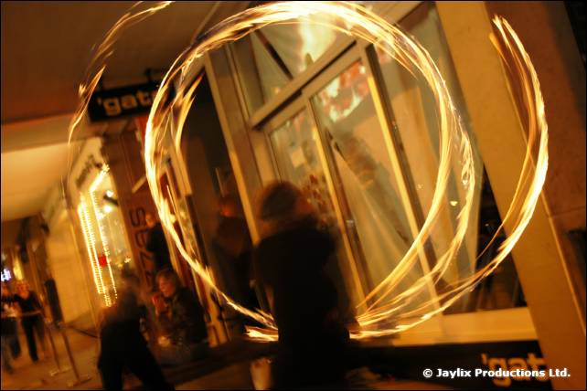 A circle of fire trails drawn in the air outside a glass shopfront at night