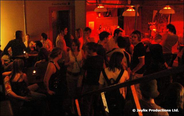 A crowded bar lit in red with people standing and talking, seen from a raised position