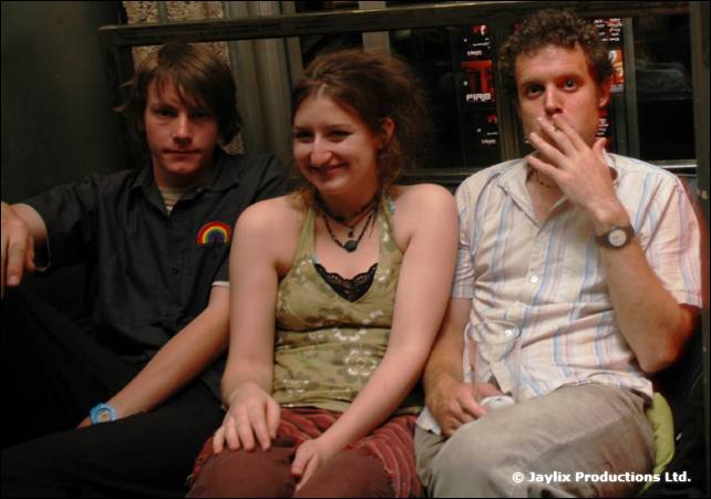 Three people sit close together on a bench, one holding a hand to their mouth