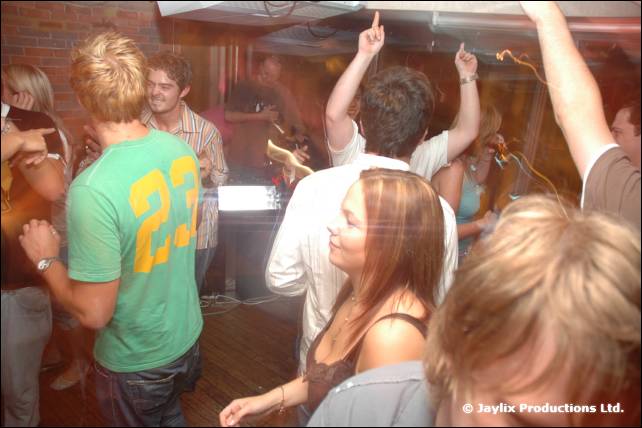 People dance in a bar, one in a green T-shirt with number 23 on the back, hands raised