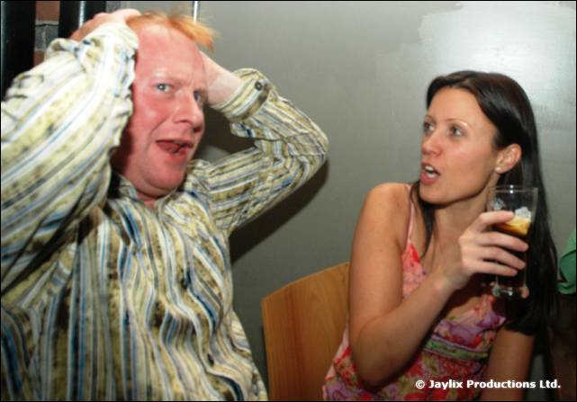 A man in a striped shirt clutches his head while a woman holding a drink looks on