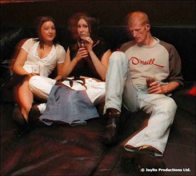 Three people sit on a dark leather sofa, one in an O'Neill top with legs stretched out