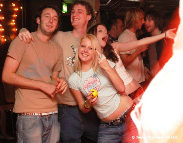 A group of friends smile and pose in a bar, one woman holding a yellow rubber duck