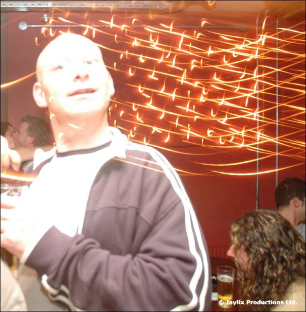 A bald person in a tracksuit top looks upward, with orange light trails on a wall behind