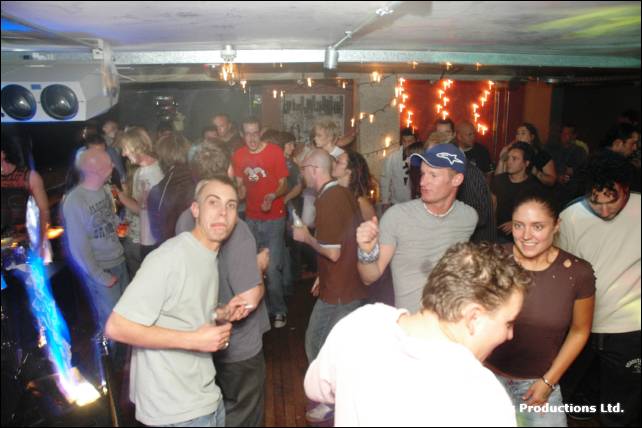A dancing crowd in a club with a projector on the ceiling and blue light at left