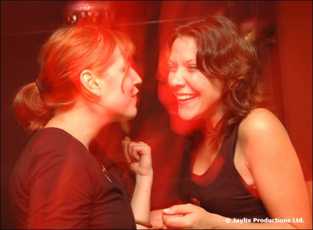 Two women laugh and talk close together in a red-lit bar