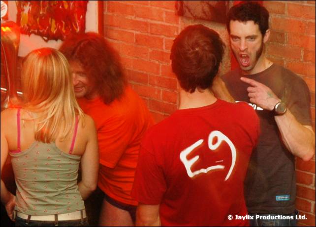 Dancers near a brick wall, one in a red E9 T-shirt, another in a dark T-shirt pointing
