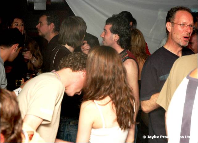 A crowded dance floor, a bald man and a woman with long hair in front, a man with glasses behind
