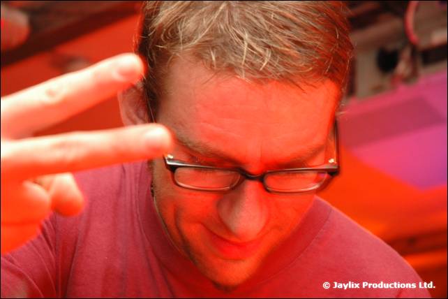 A person with glasses and short hair looks down with a hand raised, lit in red
