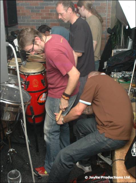 Musicians play conga drums and percussion in a corner while others stand behind