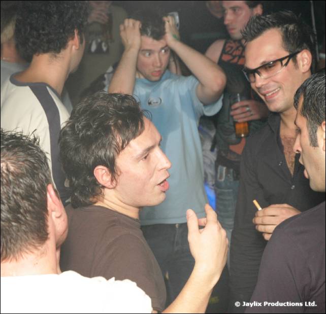 Men dance and cheer close together in a crowded, dimly lit bar