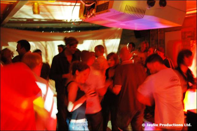 A crowd dances in a club with coloured light and a projector above