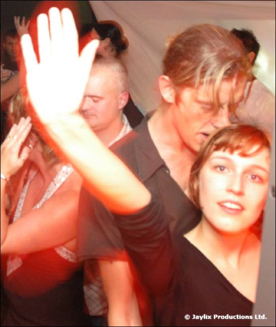 A person raises a hand in front of a crowded dance floor, with a woman in the foreground