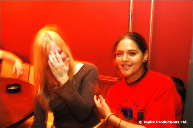 A woman covers her face with her hand beside a smiling woman in a red top, in a red booth