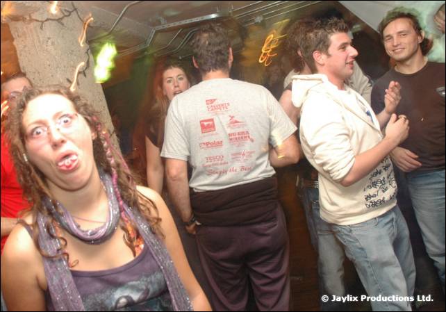 A woman with curly hair and face paint pulls a face at the camera in a crowded bar