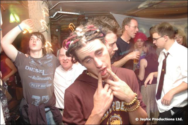 A person with dreadlocks in a Diesel T-shirt puts a finger to their mouth among a crowd