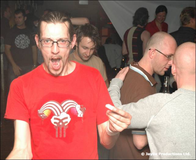 A man in a red T-shirt with a jester logo shouts and points while others stand around