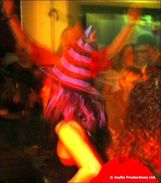 A person in a striped party hat dances with arms raised in a blurred, orange-lit room