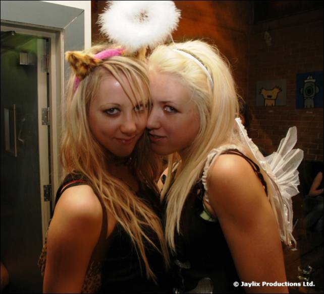 Two women pose cheek to cheek, one wearing a white halo and the other white angel wings