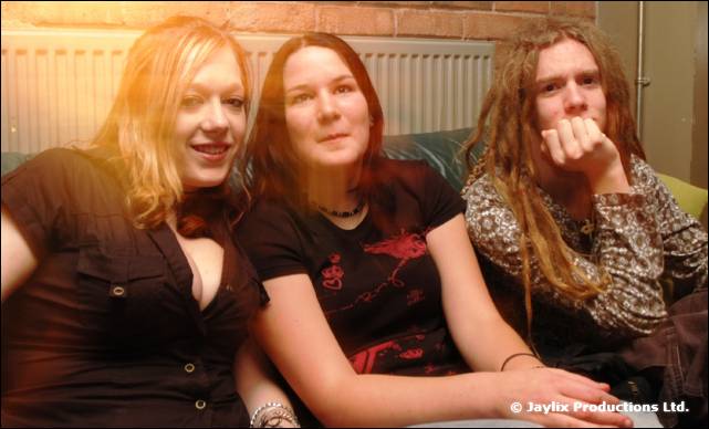 Three people sit on a sofa in front of a radiator, looking at the camera