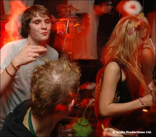 Three people crowd together in a red-lit bar, one holding a drink to their mouth