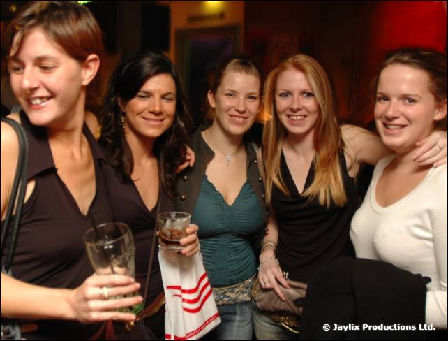 Five women smile at the camera in a bar, one holding a glass