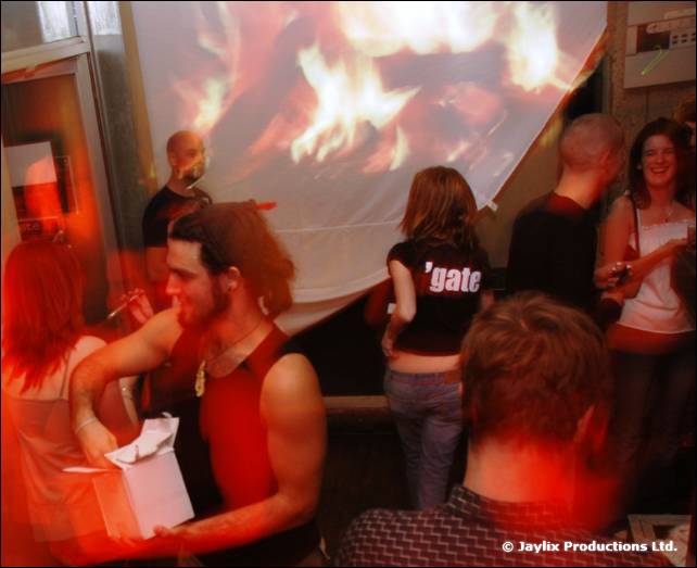 Partygoers stand in front of a projected fire image, one person holding a white gift bag