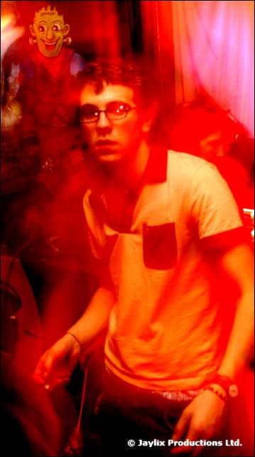 A man in glasses and a light polo shirt sits in a red haze