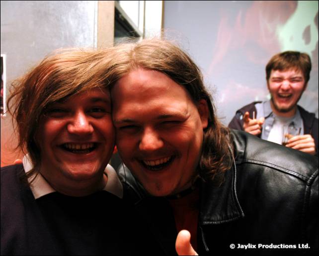 Two men press their heads together, laughing, with another man laughing behind them
