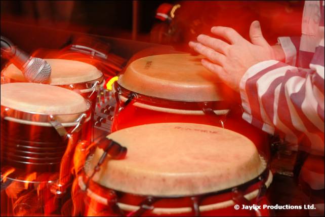 A hand reaches across conga drums, with a striped sleeve beside them