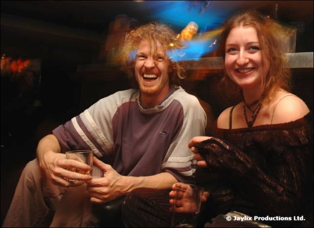 A laughing man and a smiling woman sit together holding drinks