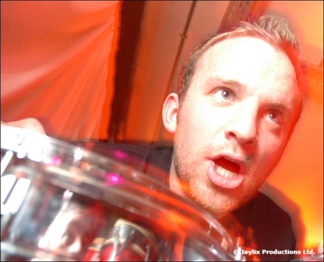 A man with a startled expression leans over a clear drum in a blur of orange light