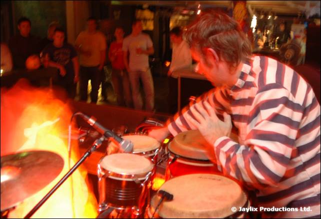 A person in a striped top plays conga drums in front of flames