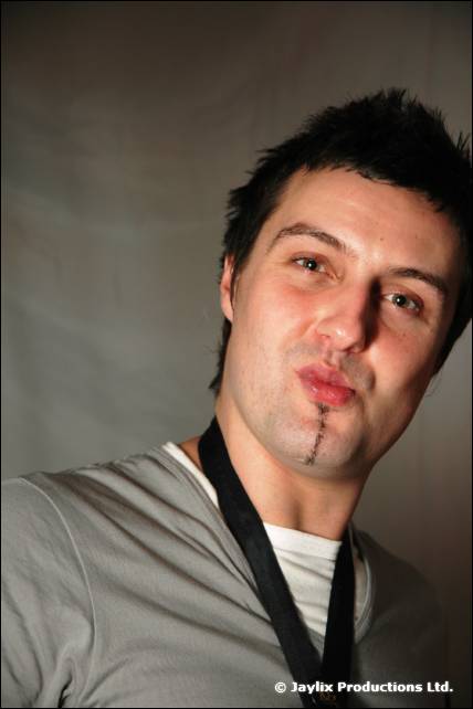 A man with spiky dark hair pouts at the camera, with a lanyard around his neck