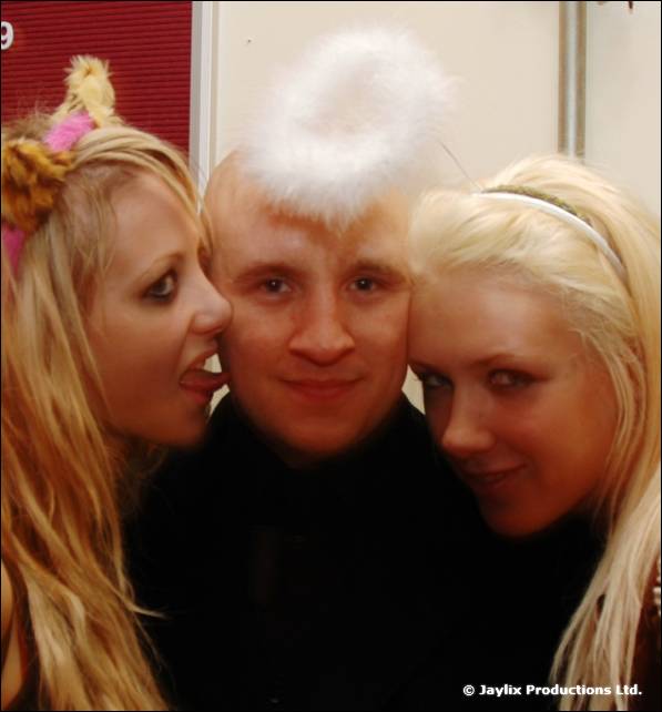 Two blonde women lean in to a man wearing a fluffy white halo on his head