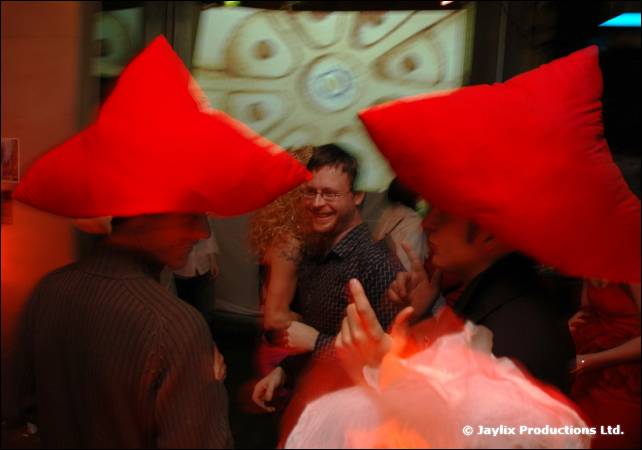 Two people wear large red hats in a dim, crowded bar