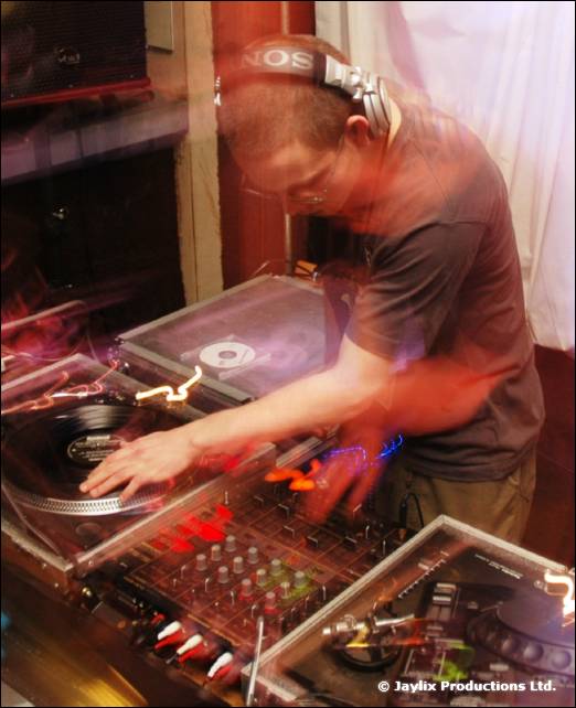 A DJ in headphones works at turntables and a mixer, blurred with movement