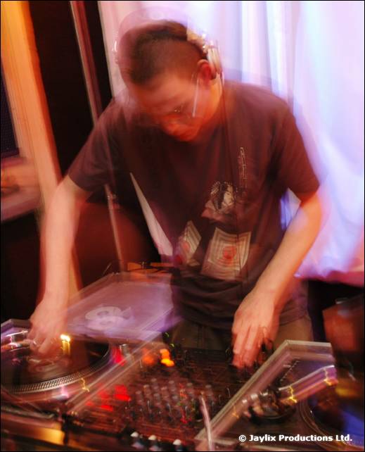 A DJ in headphones mixes at turntables, blurred with movement