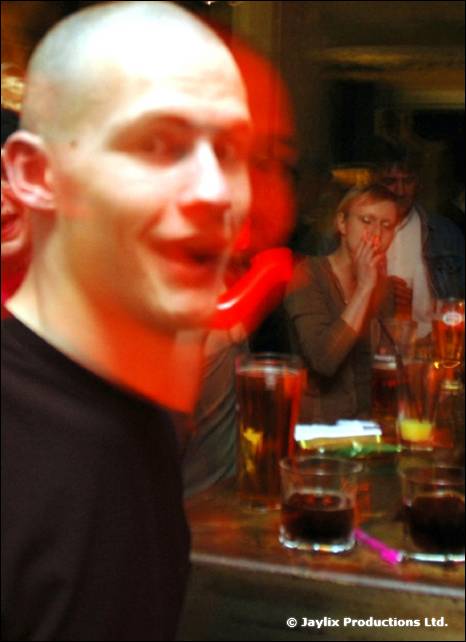 A bald man with a surprised look turns towards the camera beside a table of drinks