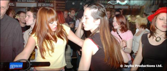 Women dance in a crowded bar, one in a yellow top and one in a black top
