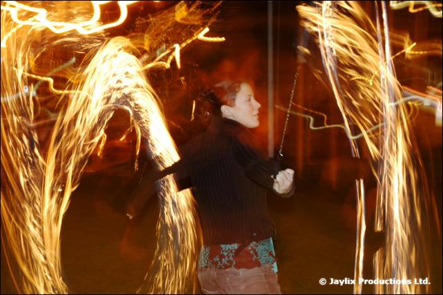 A fire performer swings trails of flame at night while a woman stands between them