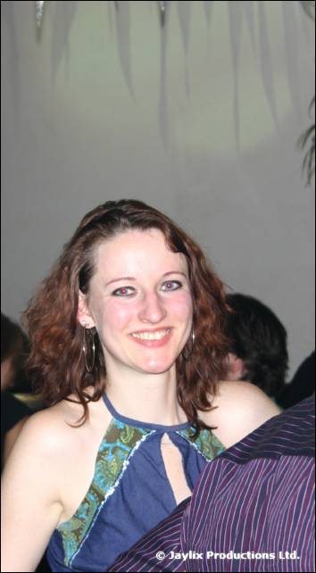 A smiling woman with curly auburn hair in a blue top looks at the camera