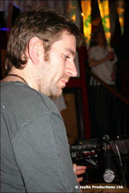A man in a grey T-shirt looks down beside audio equipment