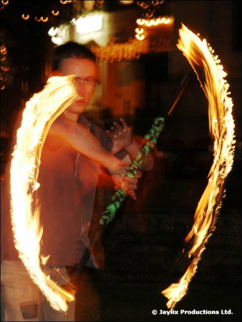 A fire performer swings two arcs of flame, with a green prop in hand