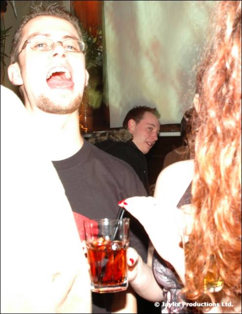 A man in glasses laughs with his mouth wide open, holding a cocktail glass