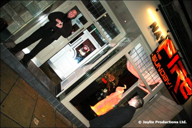 A man stands in a doorway beside a red FIRE sign on a street at night, photographed at a tilt