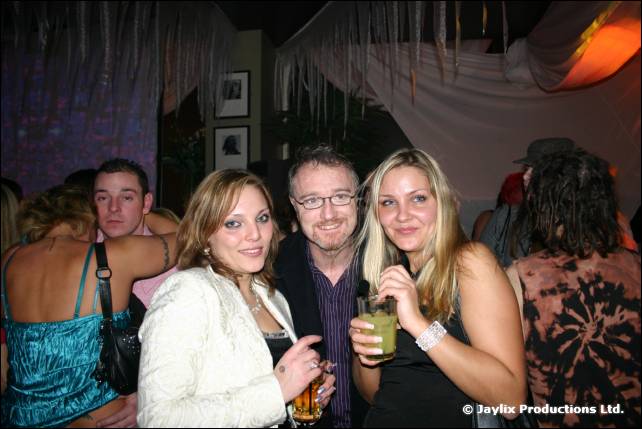 A group of people smile in a busy bar, with two men and two women in front
