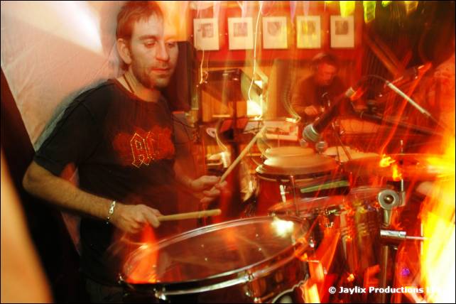A drummer in a black T-shirt plays in a blur of orange light