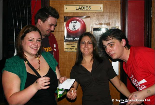 Four people pose in front of a door with a LADIES sign, two of them leaning towards each other