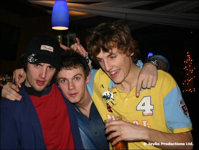 Three men in a group hug, one in a cap and one in a yellow rugby shirt with the number 4